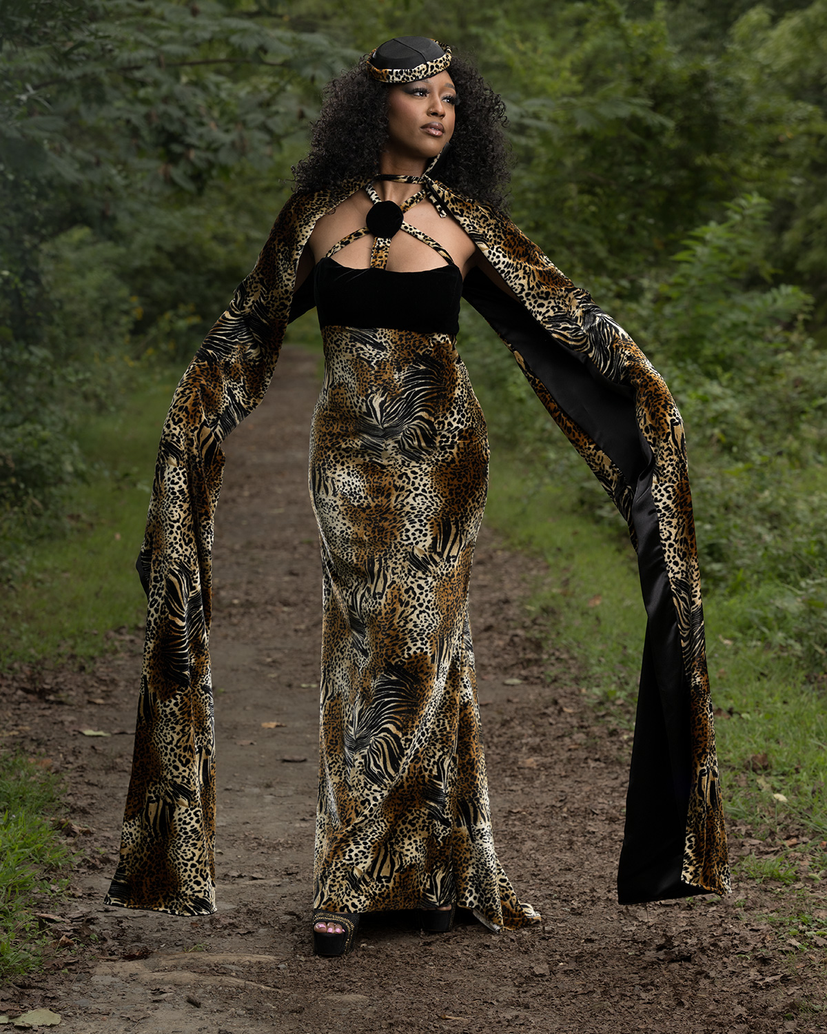 Fashion model wearing a floor-length animal print gown with dramatic flowing sleeves and black accents, posing on a wooded trail at Pump House Park in Richmond, Virginia, during an Angelias Couture fashion photography session.